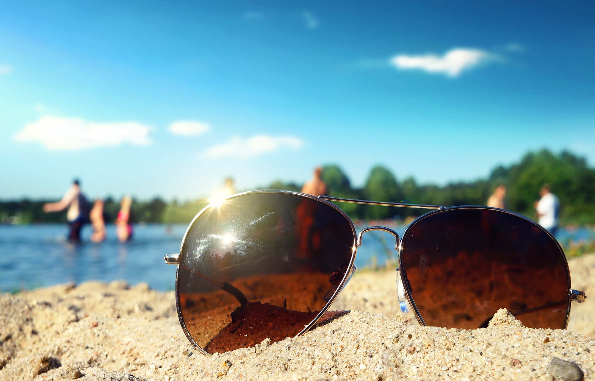 Sonnenbrille auf dem Sandstrand neben einem Badesee